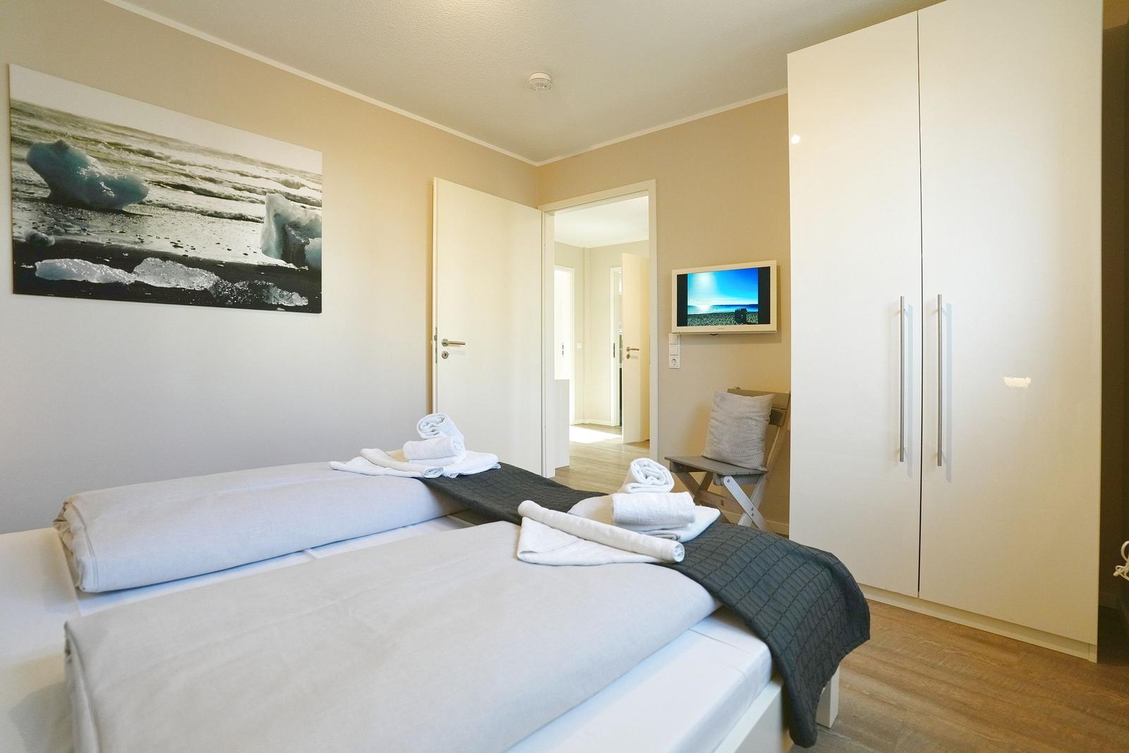 Zimmer mit Bett, Kleiderschrank und Wandbild. Fernseher an der Wand.