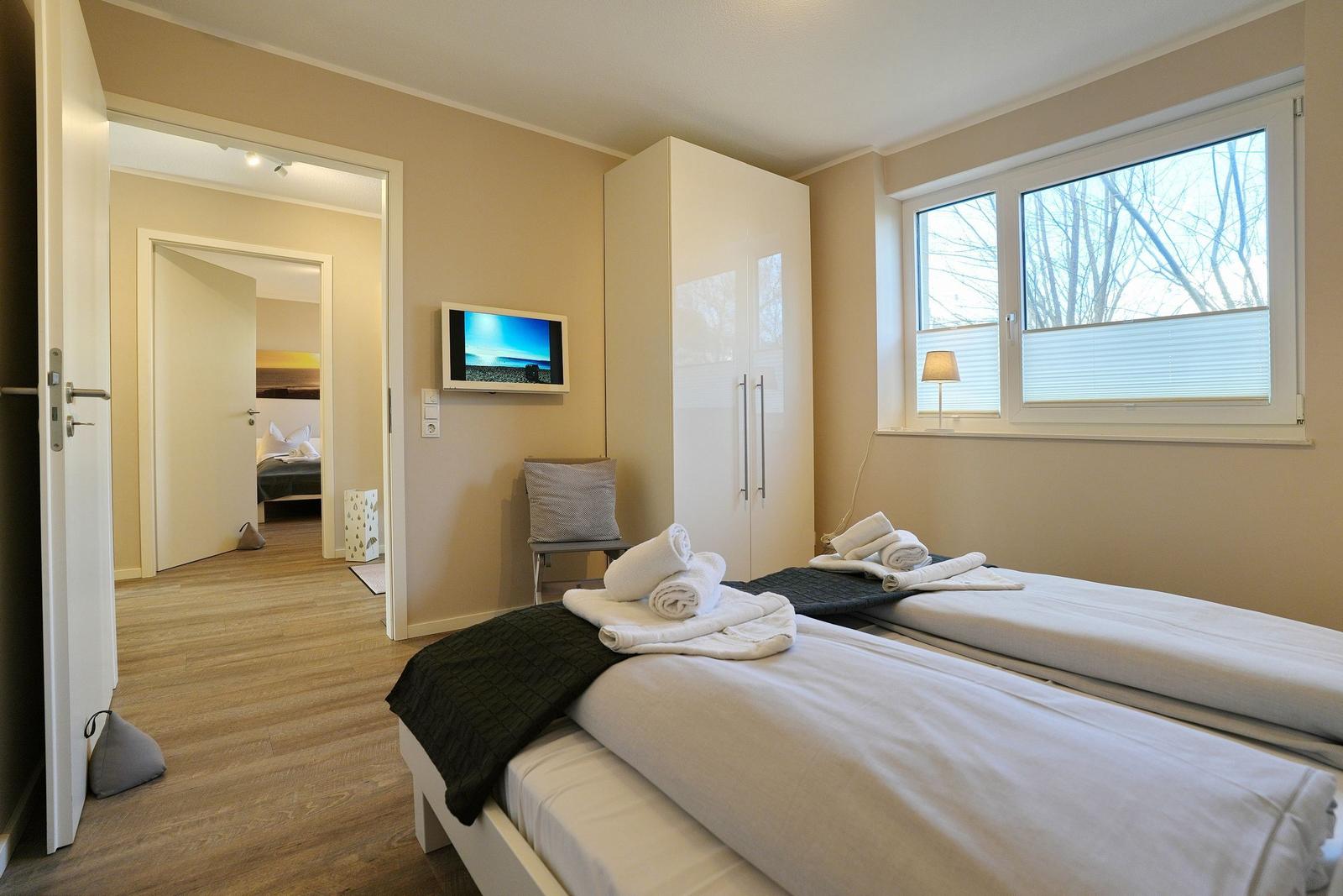 Zwei Betten mit weißen Laken und Handtüchern. Fenster mit Jalousie und Schrank.