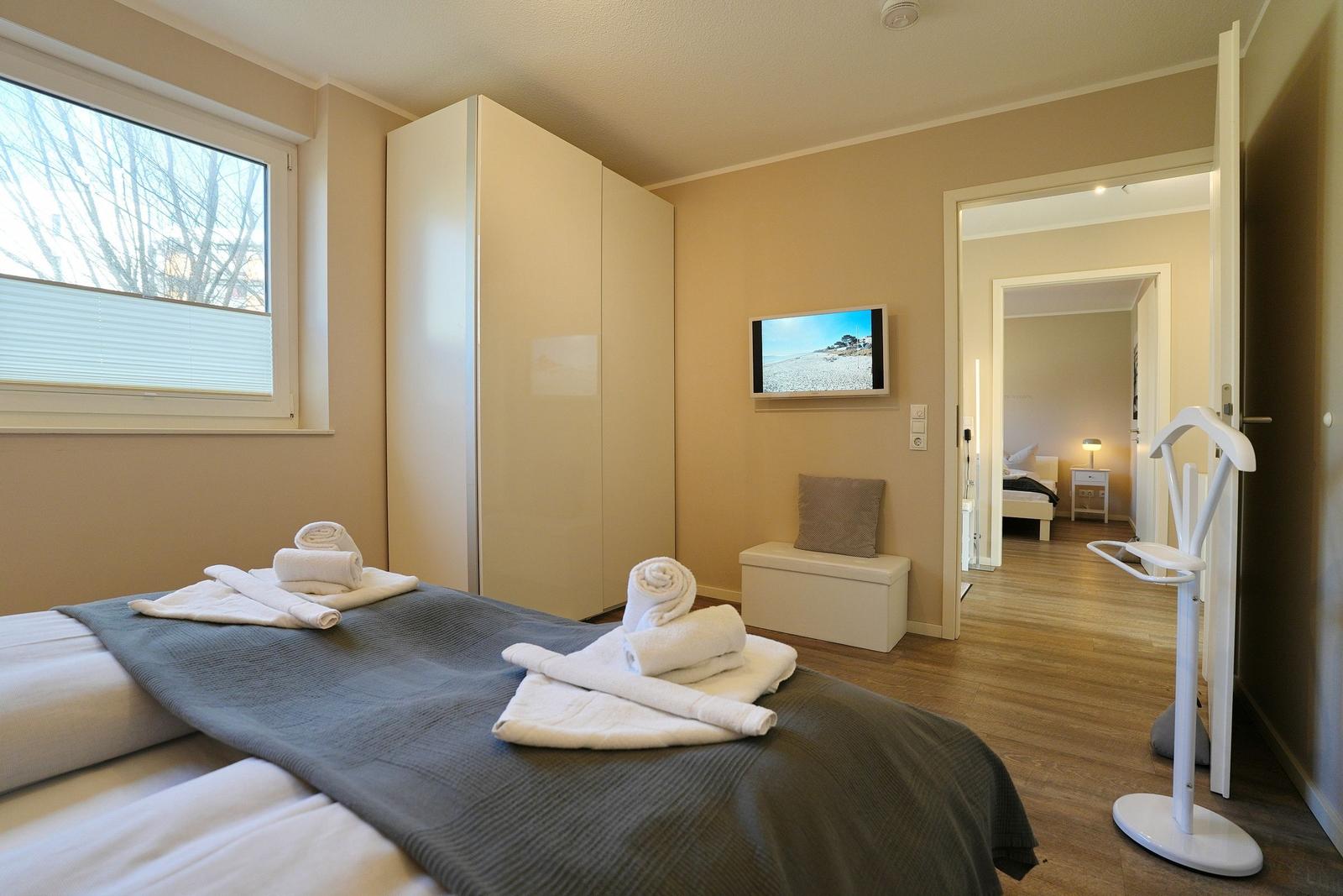 Schlafzimmer mit Bett, Kleiderschrank und Fernseher. Durchgang zu weiterem Raum.