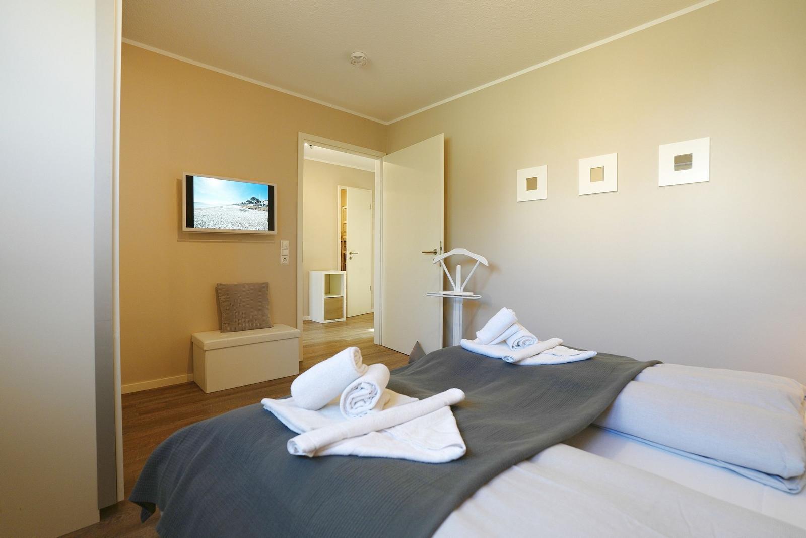 Schlafzimmer mit Bett, Handtüchern, Fernseher und Türen.