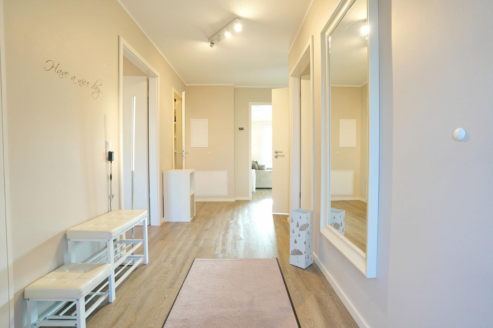 Flur mit Holzboden, Spiegel und Sitzbank. Wanddekoration und Teppich sichtbar.