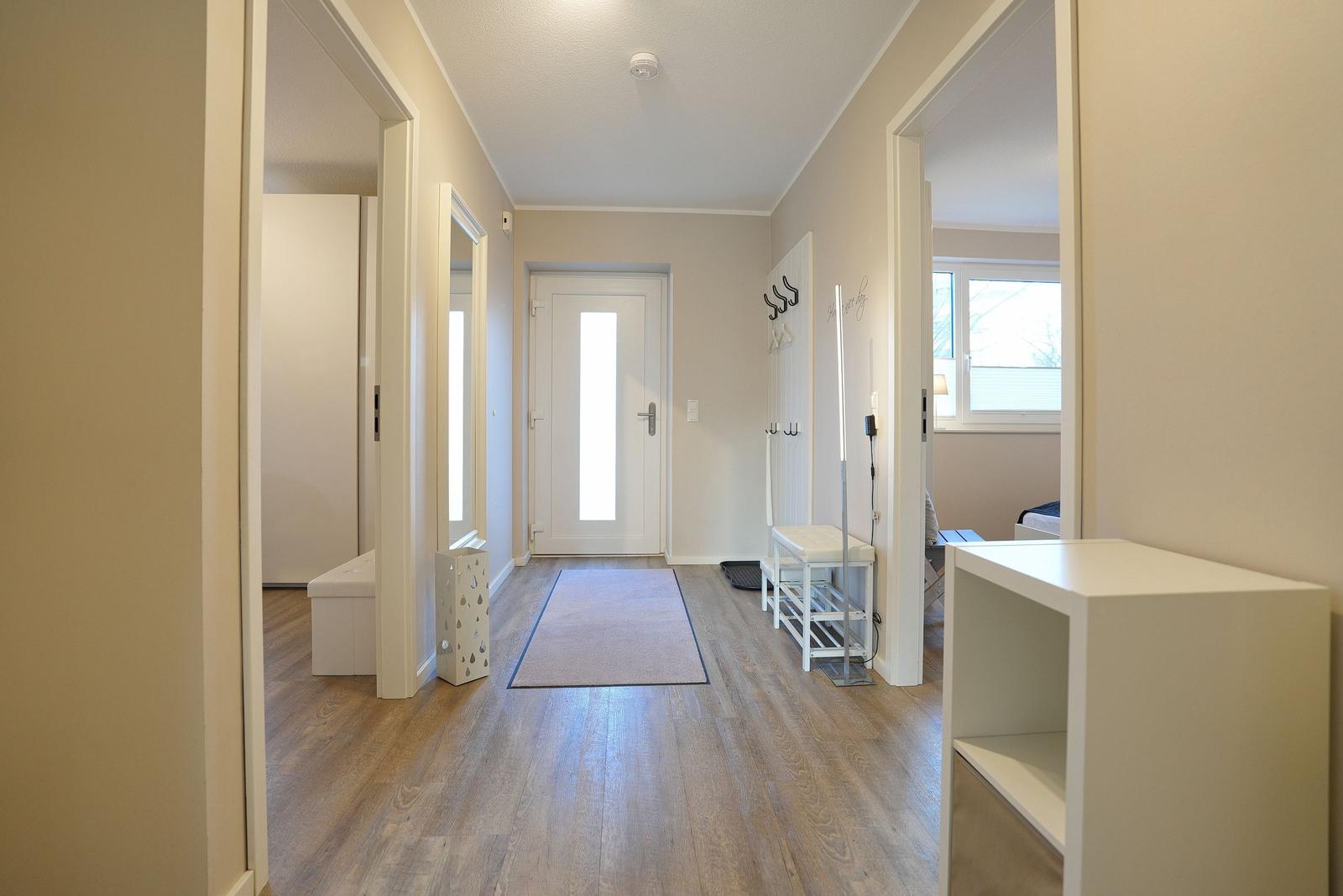 Flur mit Holzboden, Teppich und Türen zu Räumen. An der Wand hängen Haken und ein Spiegel.