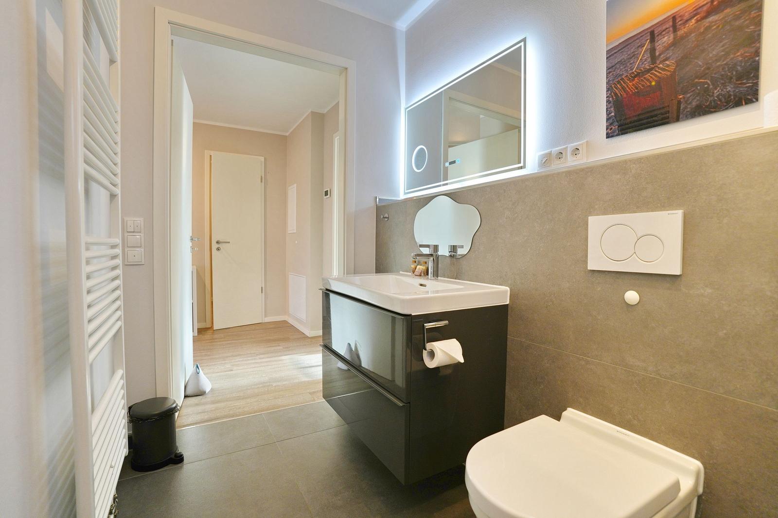 Bad mit Waschtisch, Toilette und Heizung. Spiegel und Wandbild sind sichtbar.