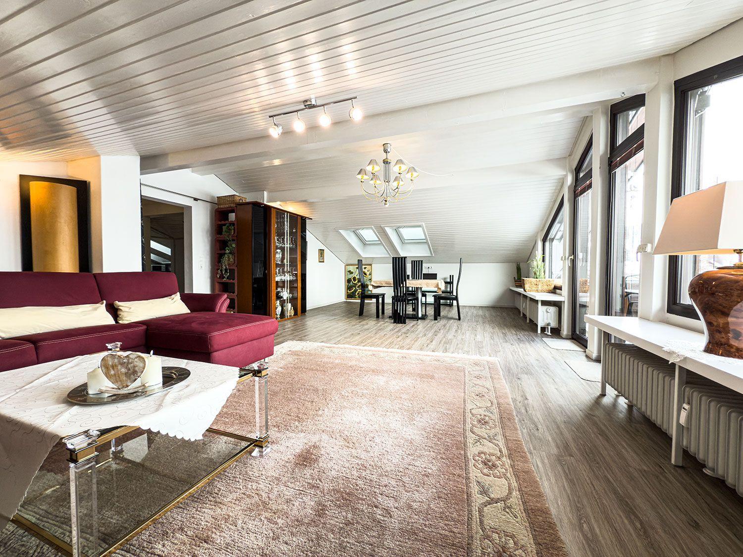 Wohn- und Essbereich mit rotem Sofa, Holzboden und Dachfenstern.