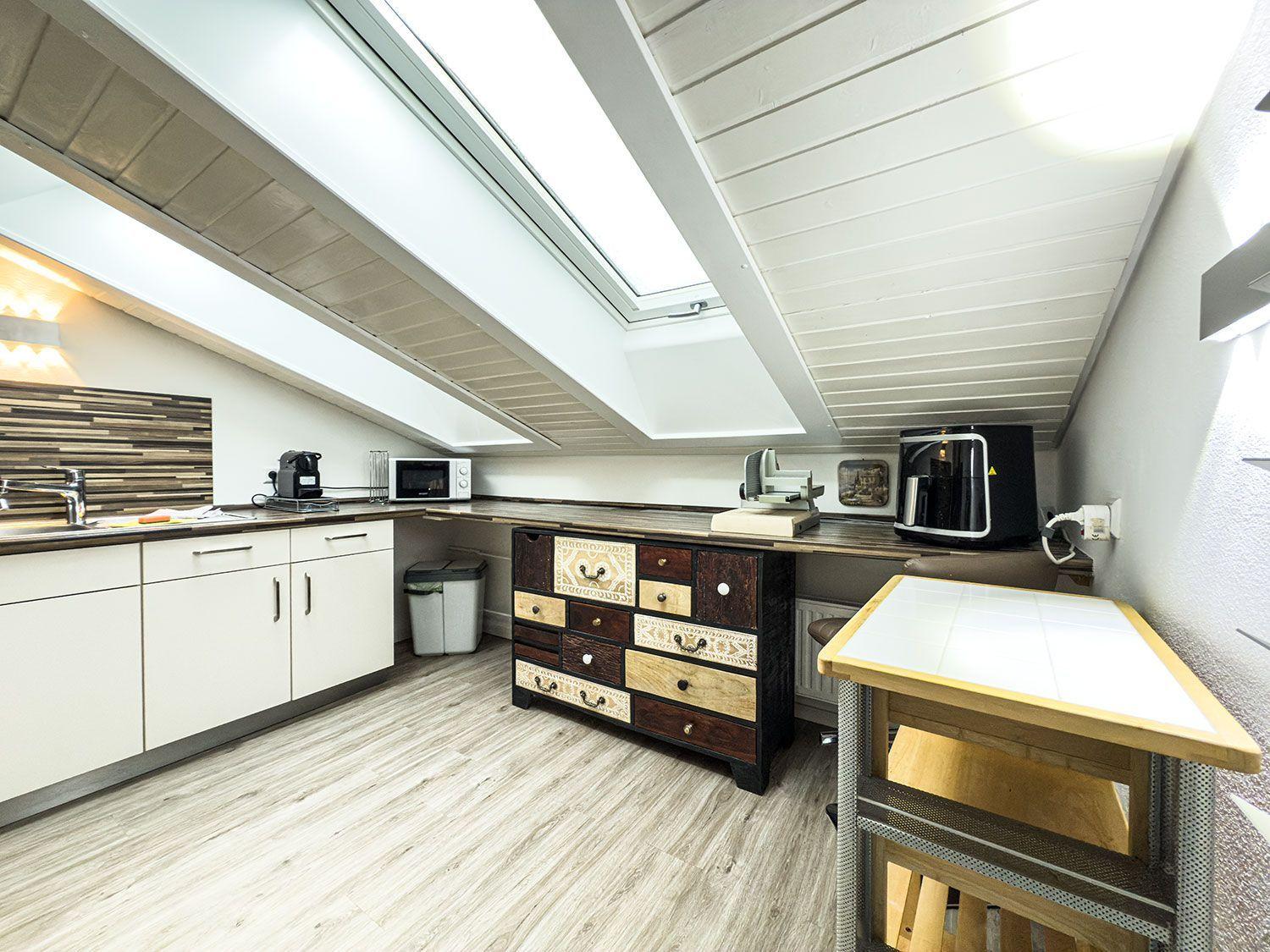 Küche mit Dachschrägen, Arbeitsplatte, Kühlschrank und Schrank.