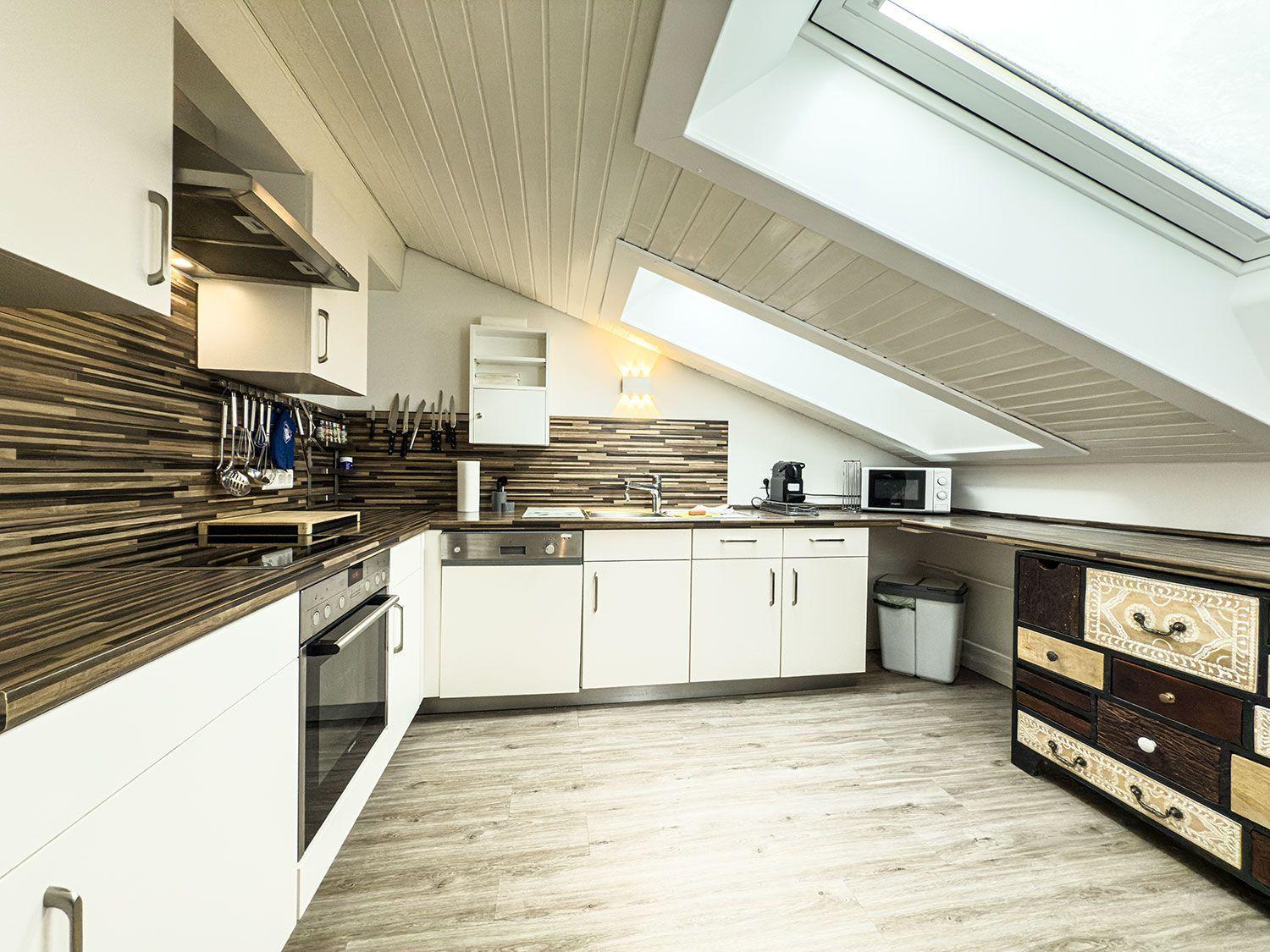 Küche mit weißen Schränken, Holzoptik und Dachfenster.