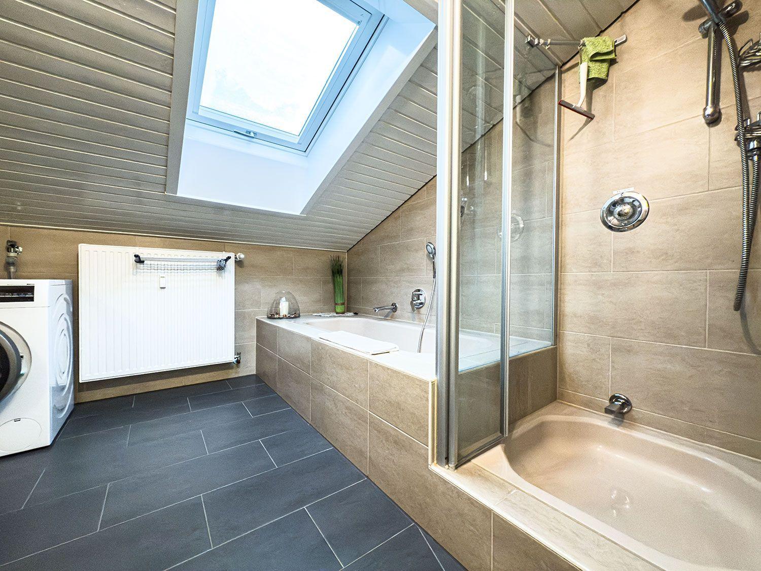 Badezimmer mit Dusche, Badewanne und Waschmaschine unter Dachschrägen.