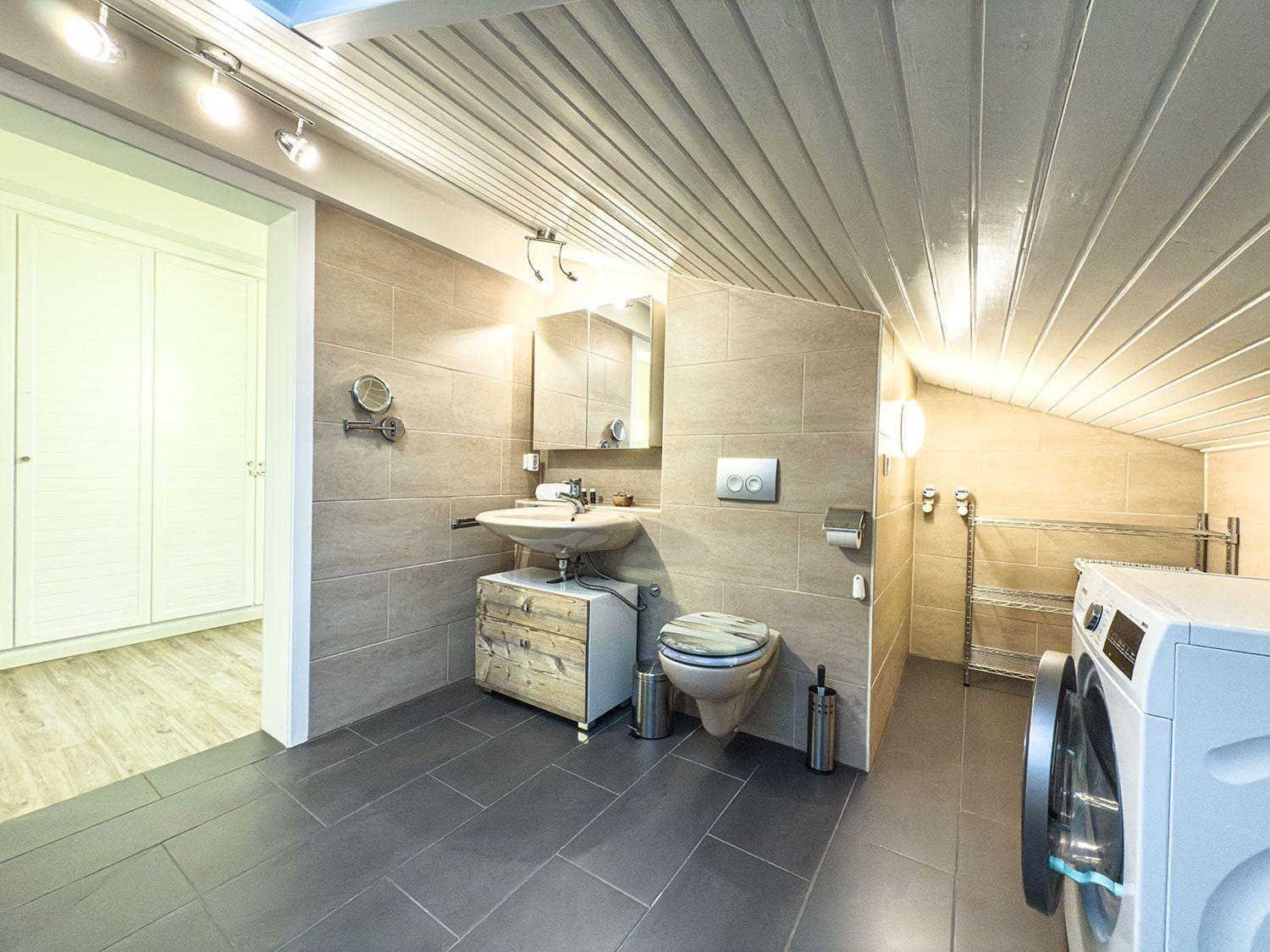 Badezimmer mit Waschmaschine, Toilette und Spiegel. Holzoptik und Steinfliesen.