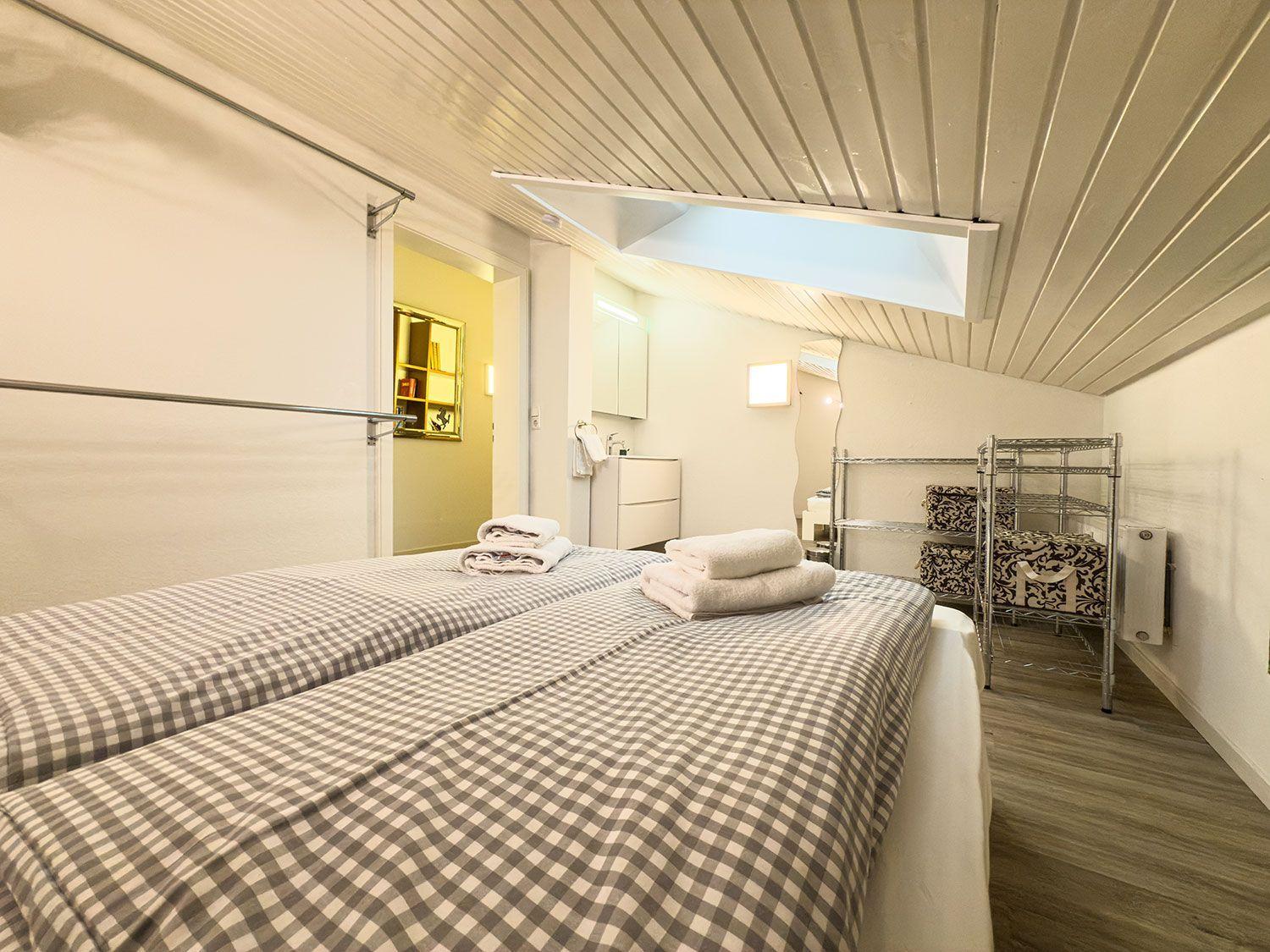 Zwei Betten mit karierten Bettdecken, Doppelwaschbecken und Aufbewahrungskörbe.