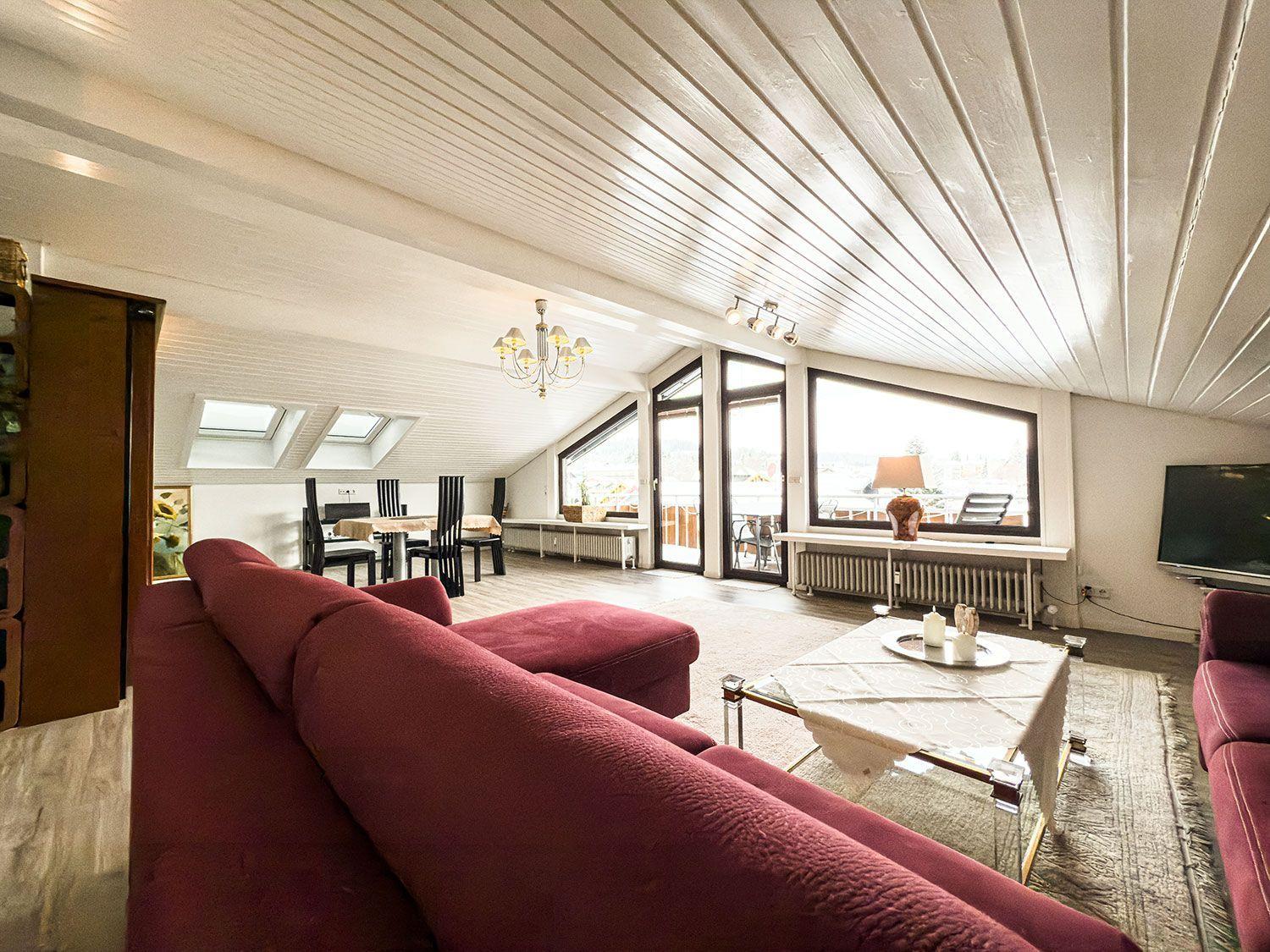 Wohnbereich mit rotem Sofa, Glas-Tisch und großen Fenstern.