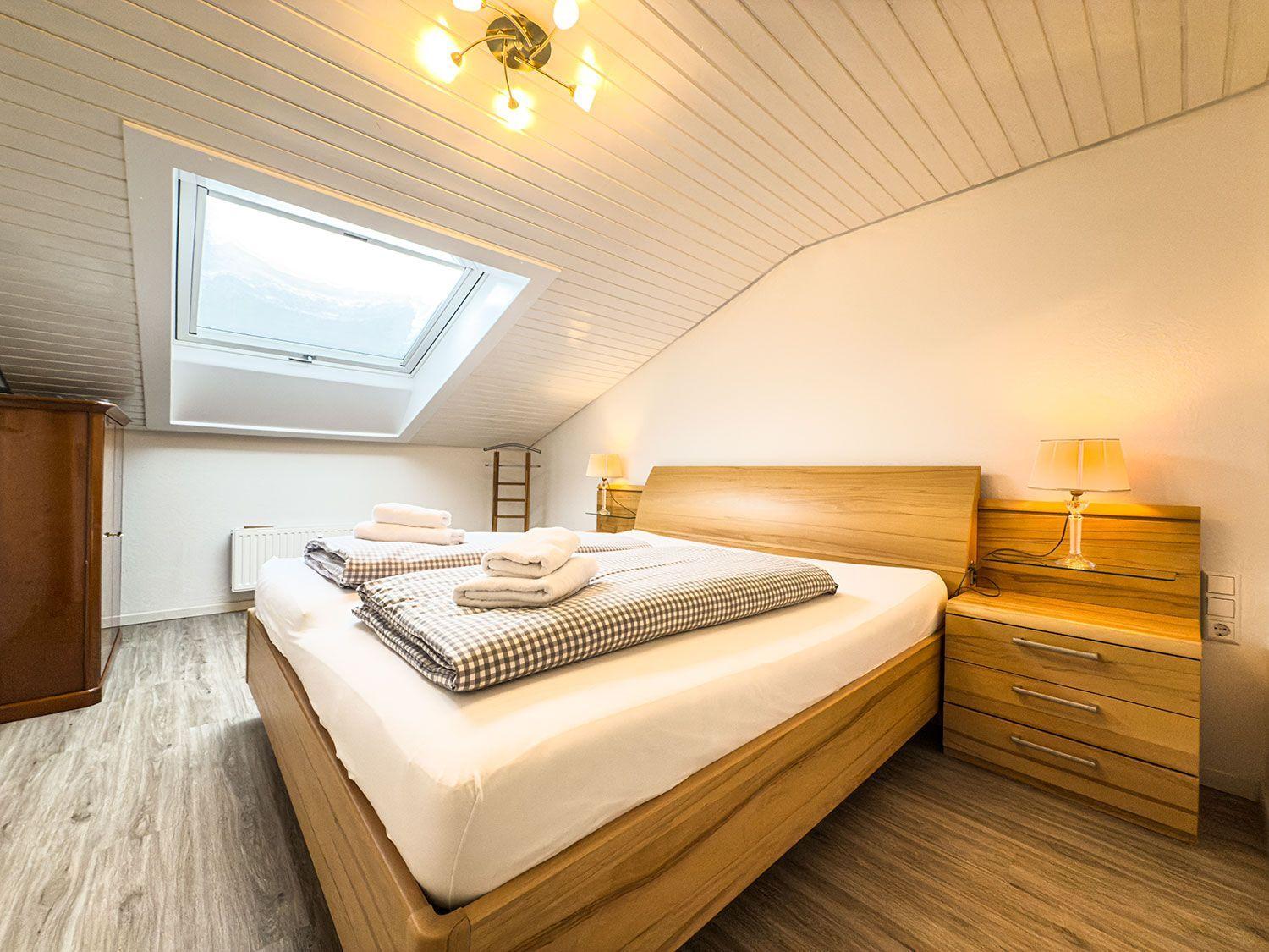 Schlafzimmer mit Dachfenster, Holzbett und Nachttisch mit Lampe.