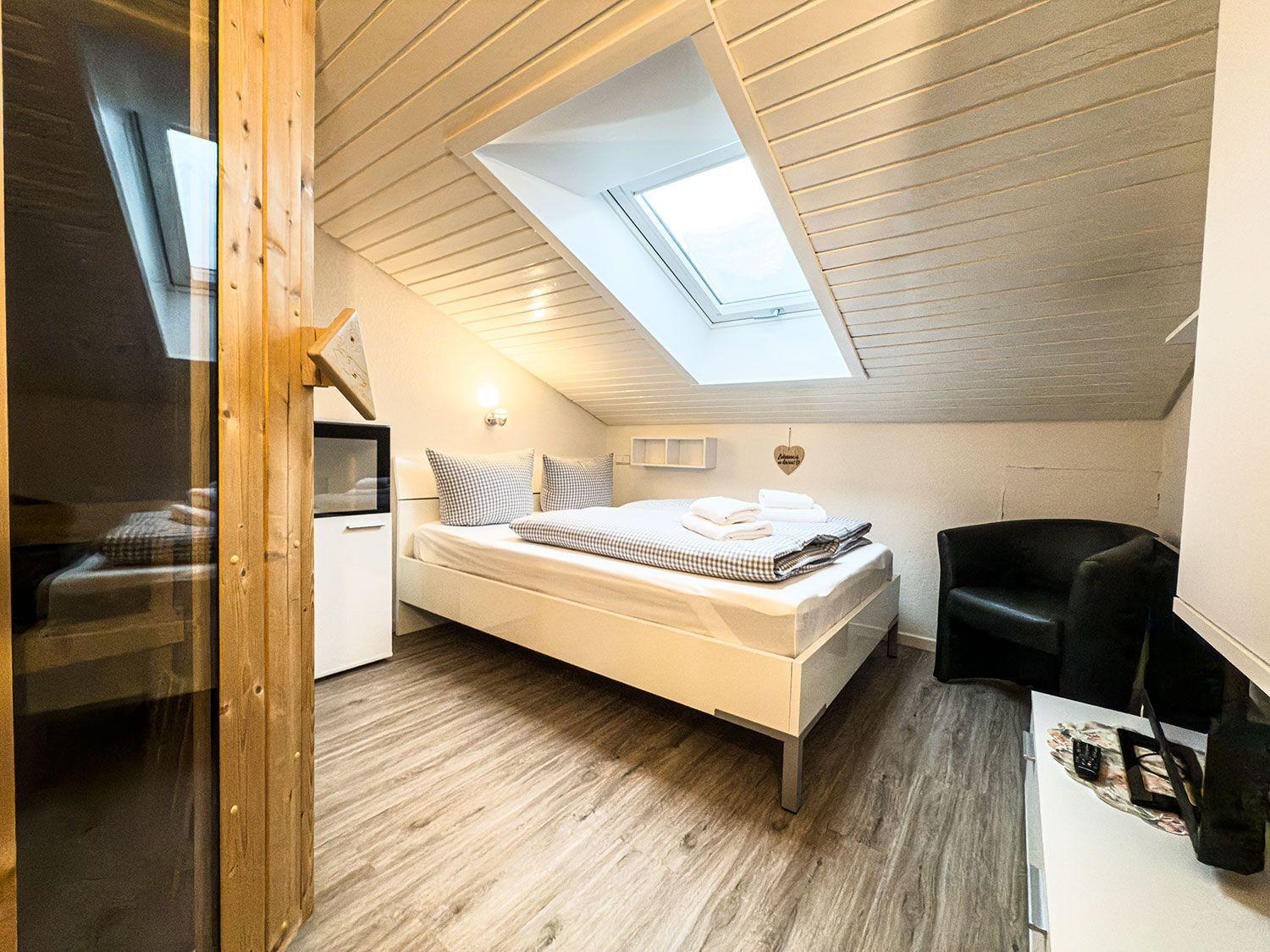 Schlafzimmer mit Dachschrägen, Dachfenster, Bett, Sessel und Schrank.