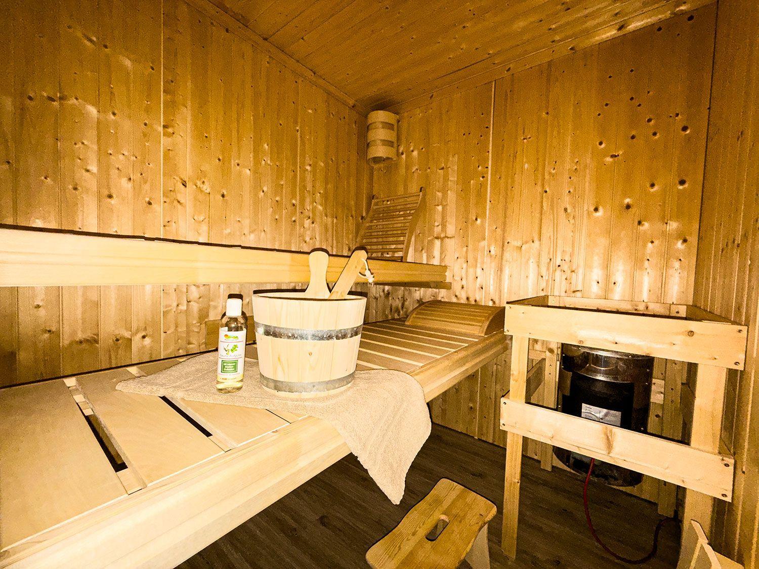 Sauna mit Holzbank, Eimer und Ölflasche. Heizung unter Holzgestell.
