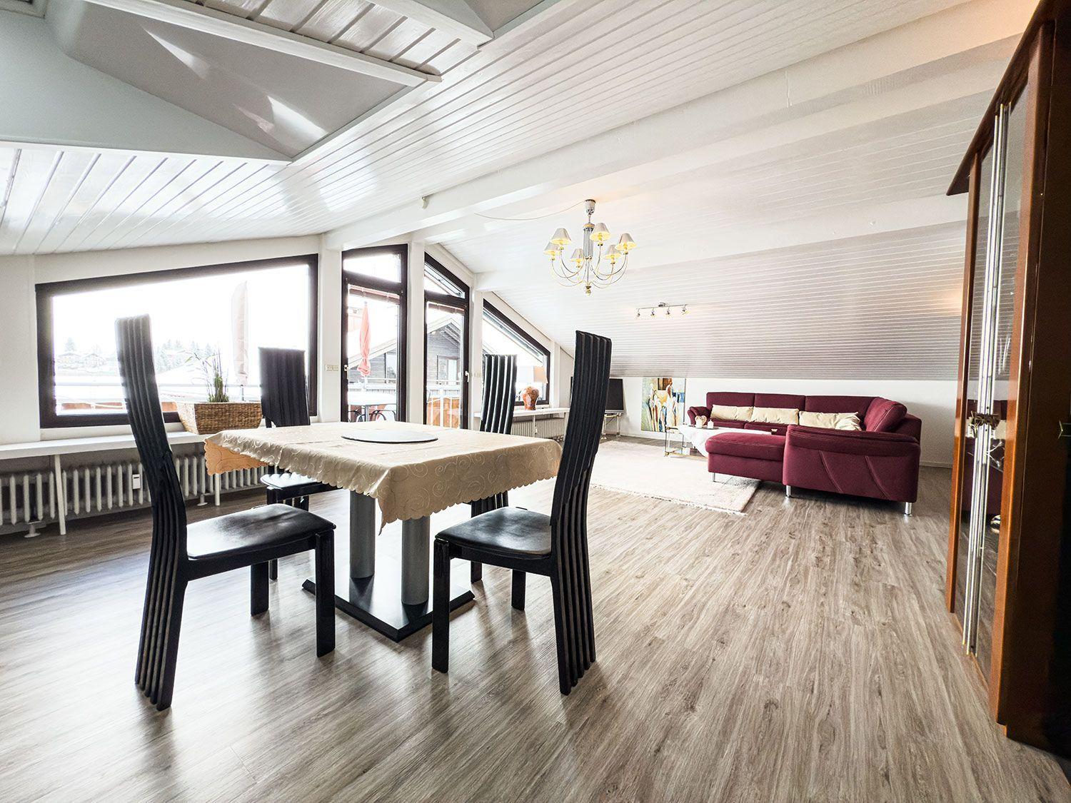 Essbereich mit Tisch und Stühlen, Wohnbereich mit rotem Sofa und Holzboden.