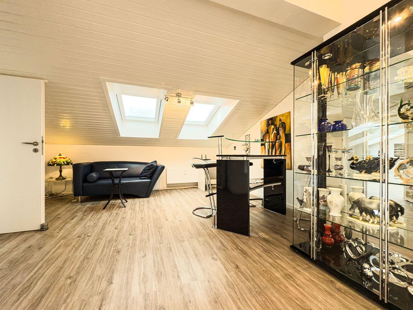 Wohnraum mit Sofa, Bar und Glasvitrine unter Dachschrägen.
