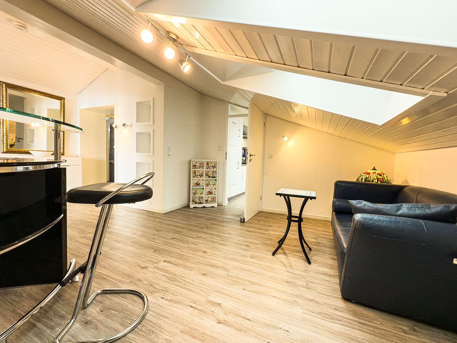 Wohnbereich mit Sofa, Tisch und Barhocker unter Holzdecke.