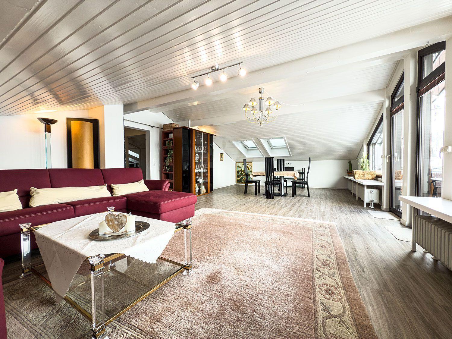 Wohn- und Essbereich mit rotem Sofa, Glas-Tisch und Holzboden.