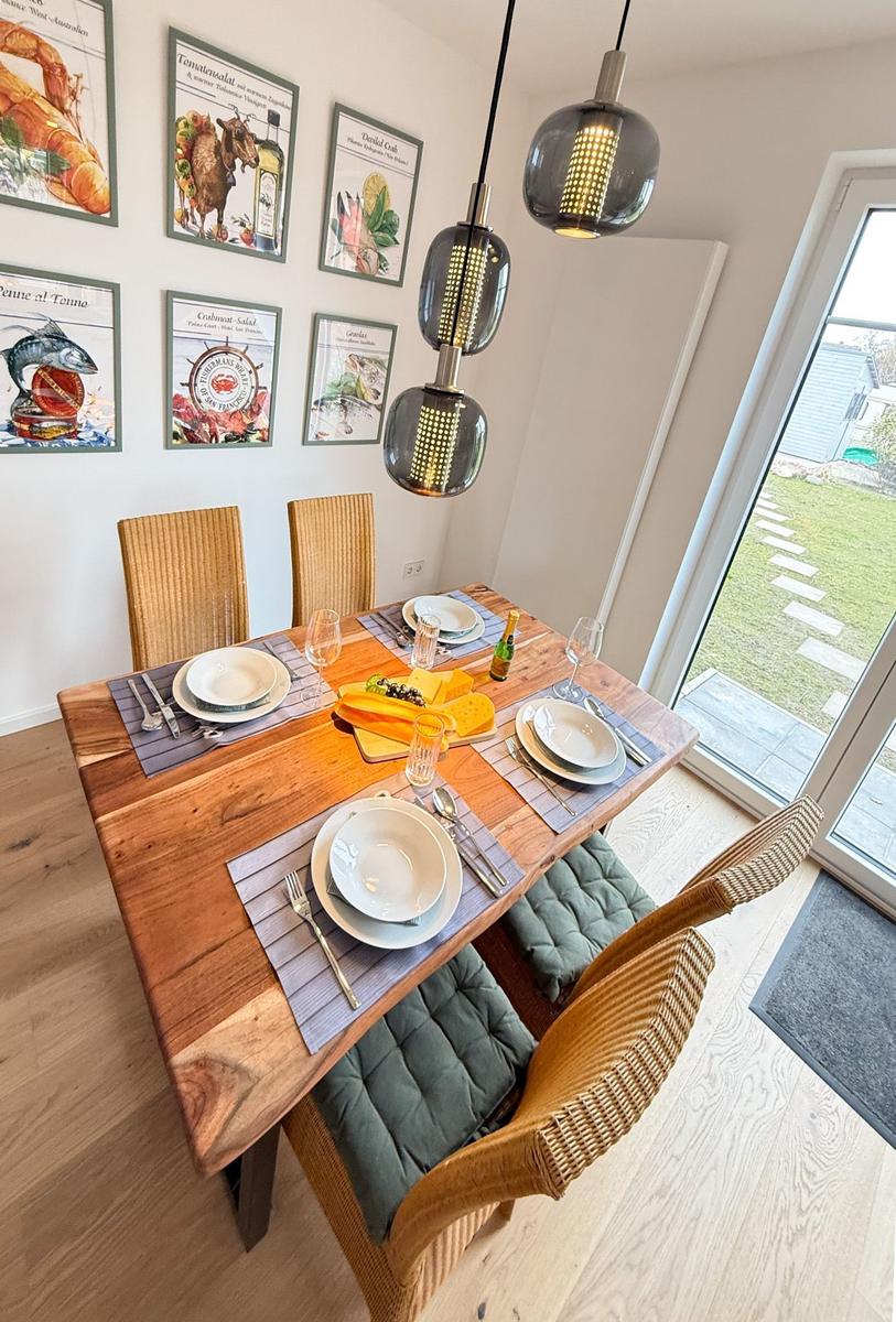 Dining room with wooden table, chairs, and wall art. Outside is a garden.
