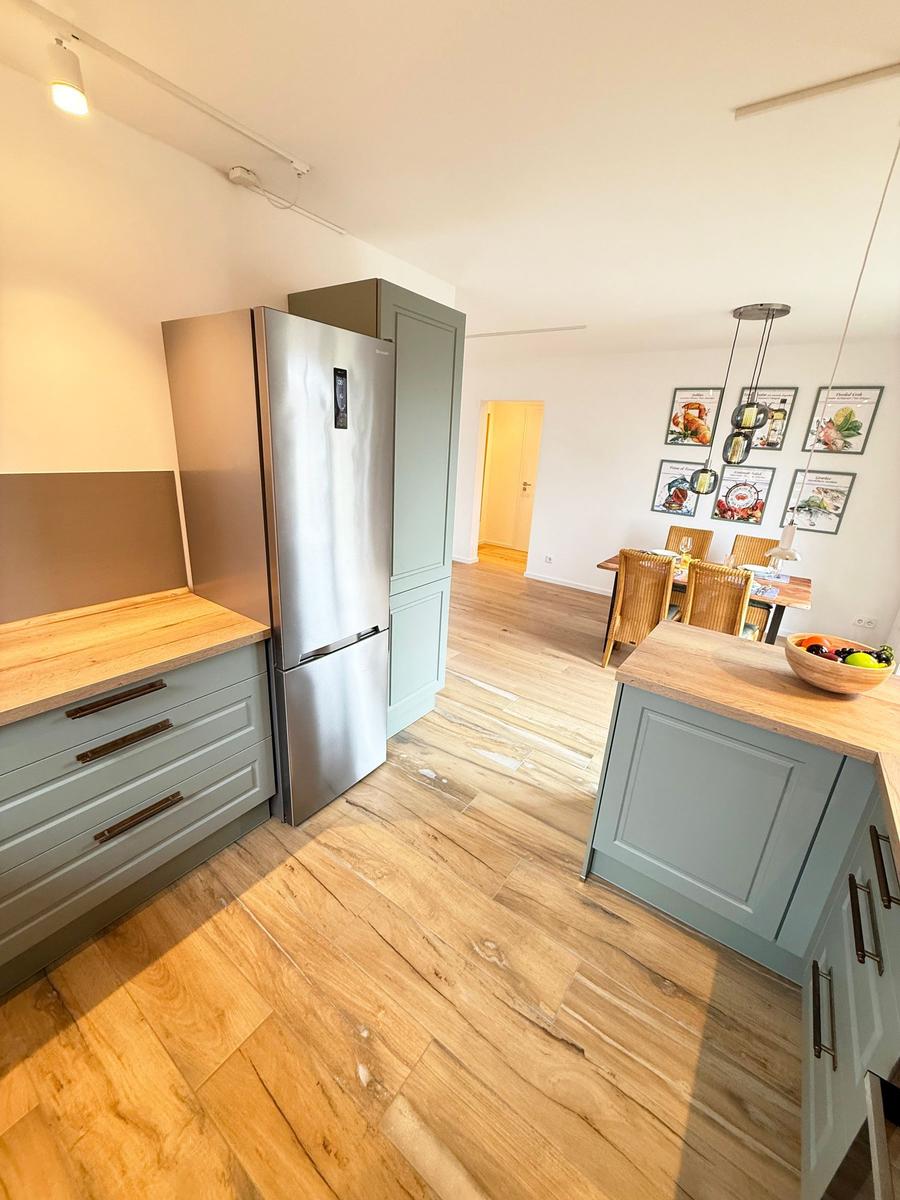 Kitchen with wooden floor, stainless steel refrigerator, and dining area with table and chairs.