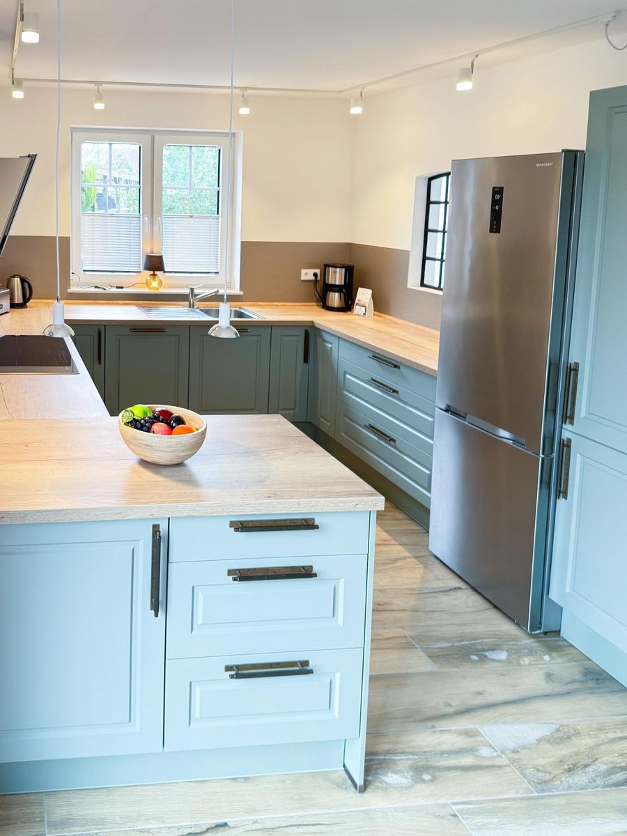 Modern kitchen with island, wooden surfaces, and stainless steel refrigerator.