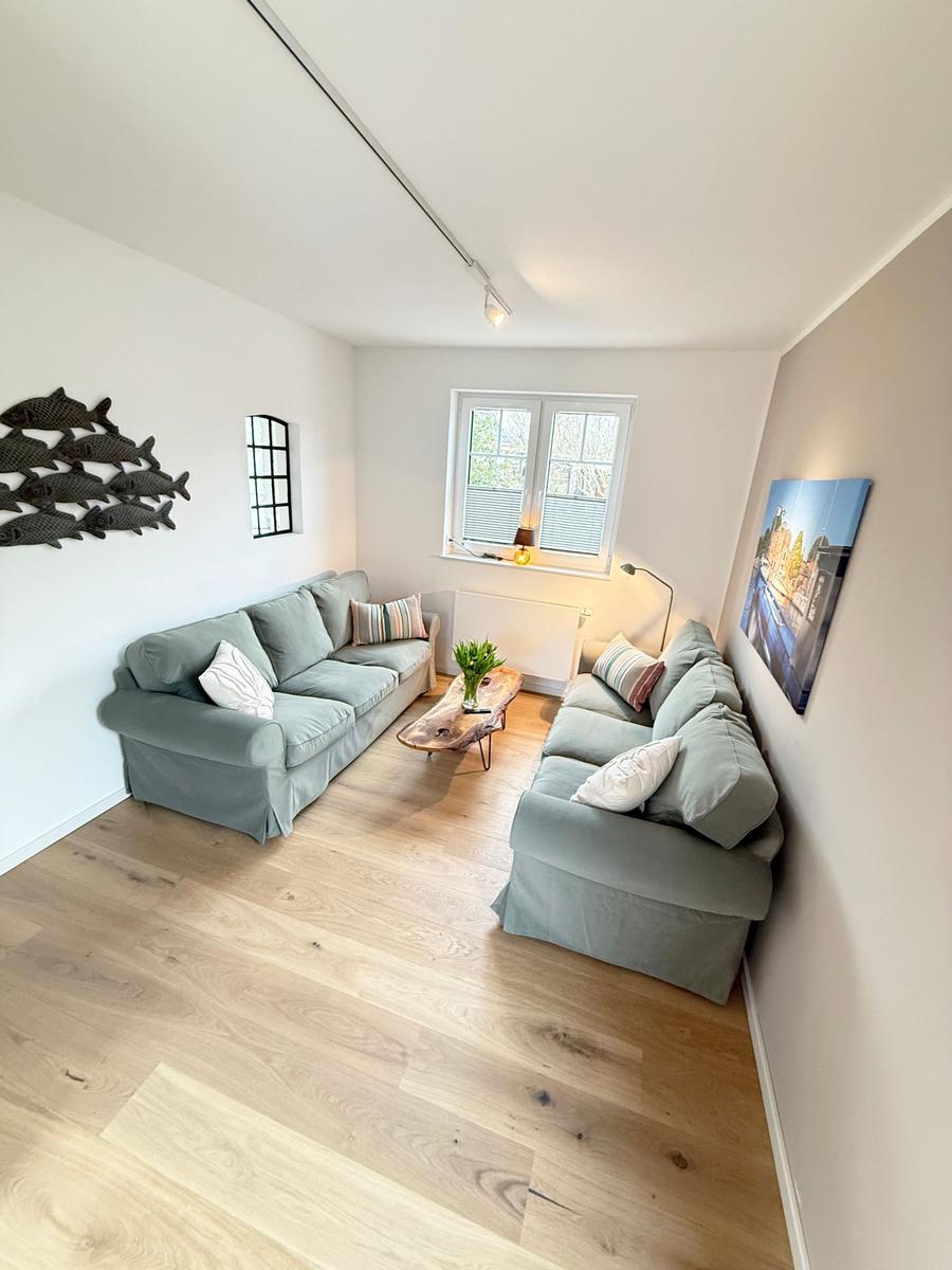Living room with two sofas, wooden floor, and window. Wall decor and table.