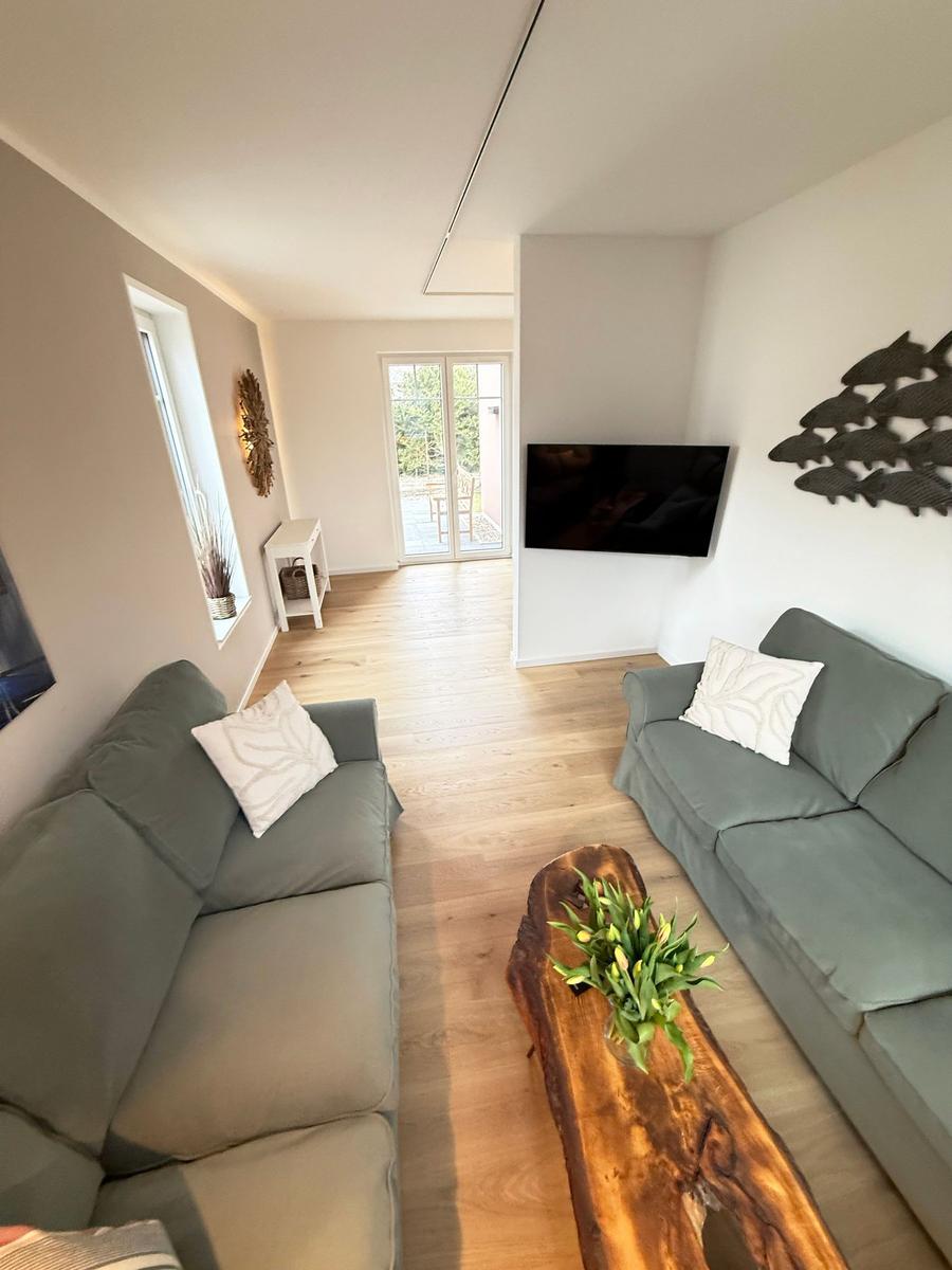 Living room with two sofas, wooden table, and TV. Corridor to terrace.