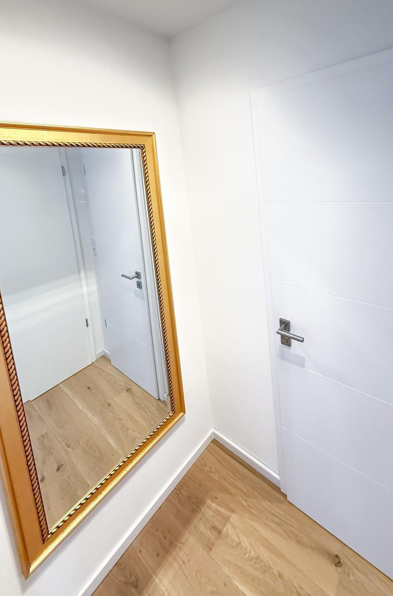 Hallway with gold-framed mirror and white doors on light wood floor