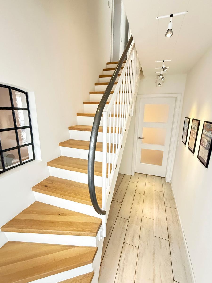 Staircase with wooden steps, white railings, and floor. Pictures hang on the wall.