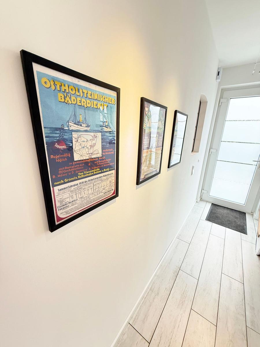 Hallway with wall pictures and wooden floor. Door leads outside.