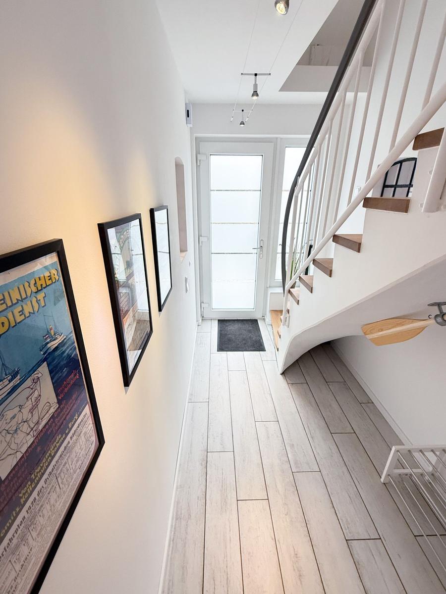 Hallway with wooden floor, staircase, and wall art. Door to outdoor area.