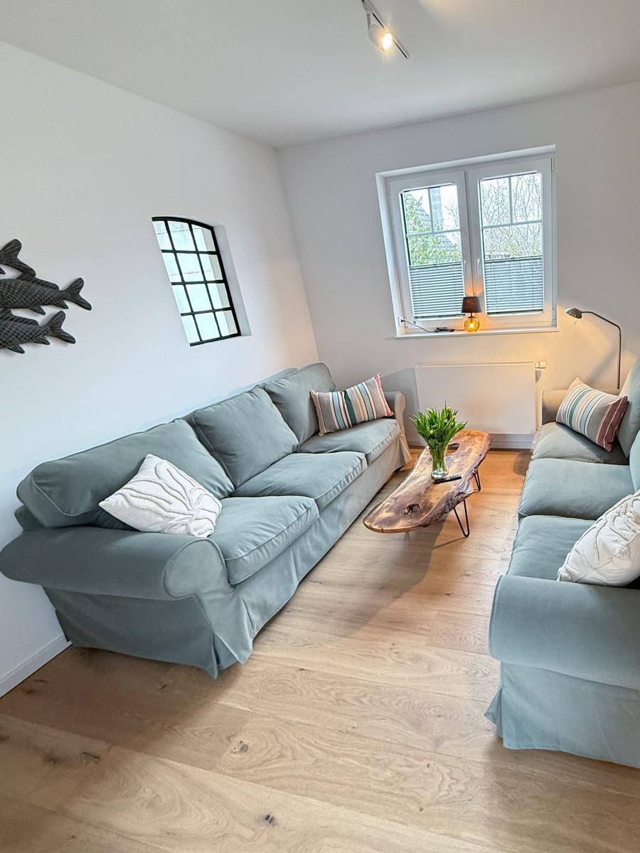 Living room with two sofas, wooden floor, and windows. Table with flowers and wall decoration.