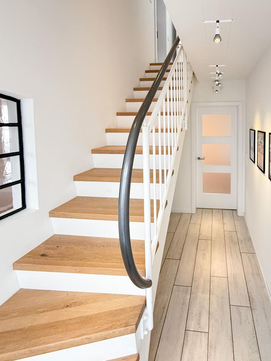 Stairs with wooden steps and white railing lead upstairs. Hallway with wooden flooring and door.