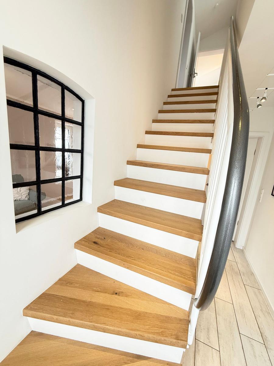Wooden staircase with white railing and black-framed window in the background.