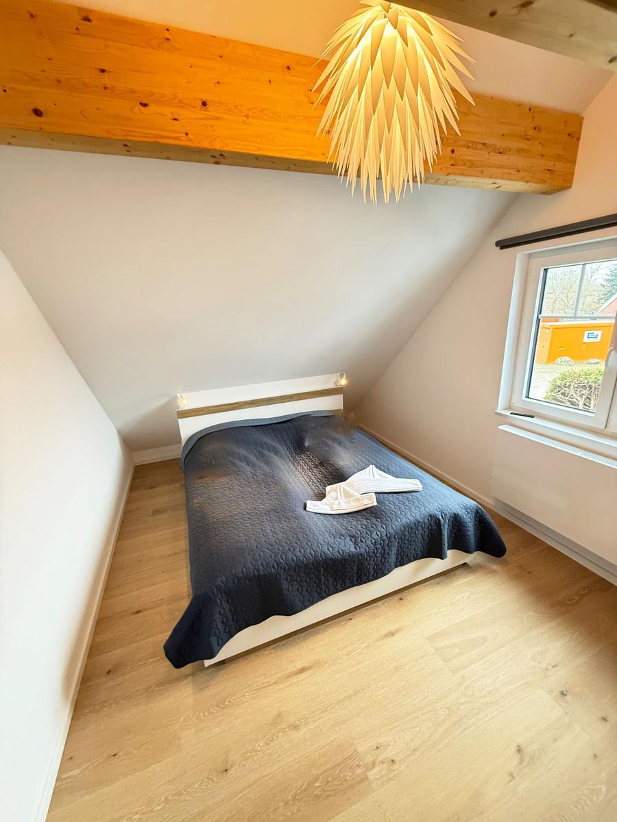 Bedroom with sloped ceiling, wooden floor, and bed with dark bedding.