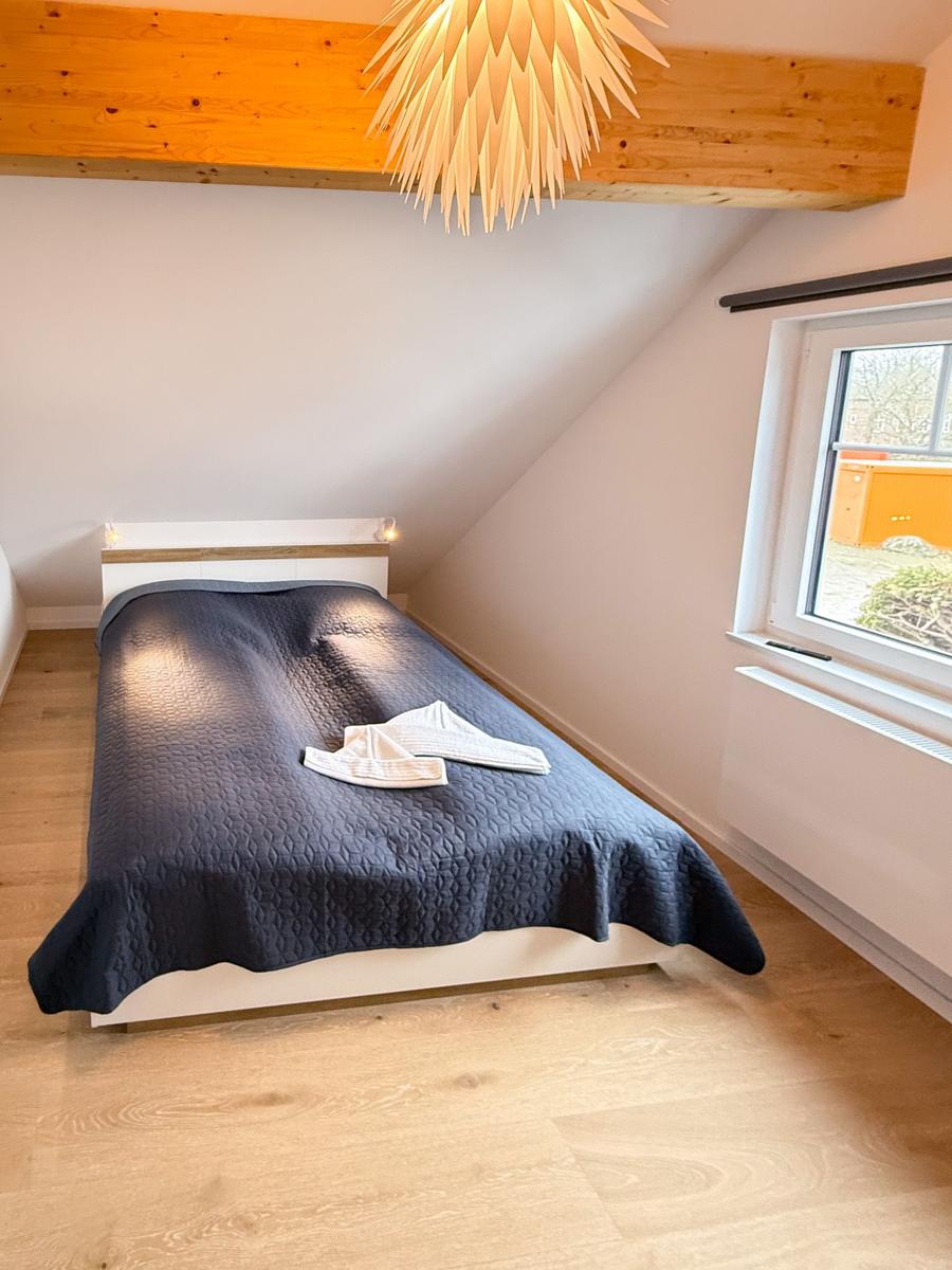 Bedroom with sloped ceiling, bed, window, and wooden beam.