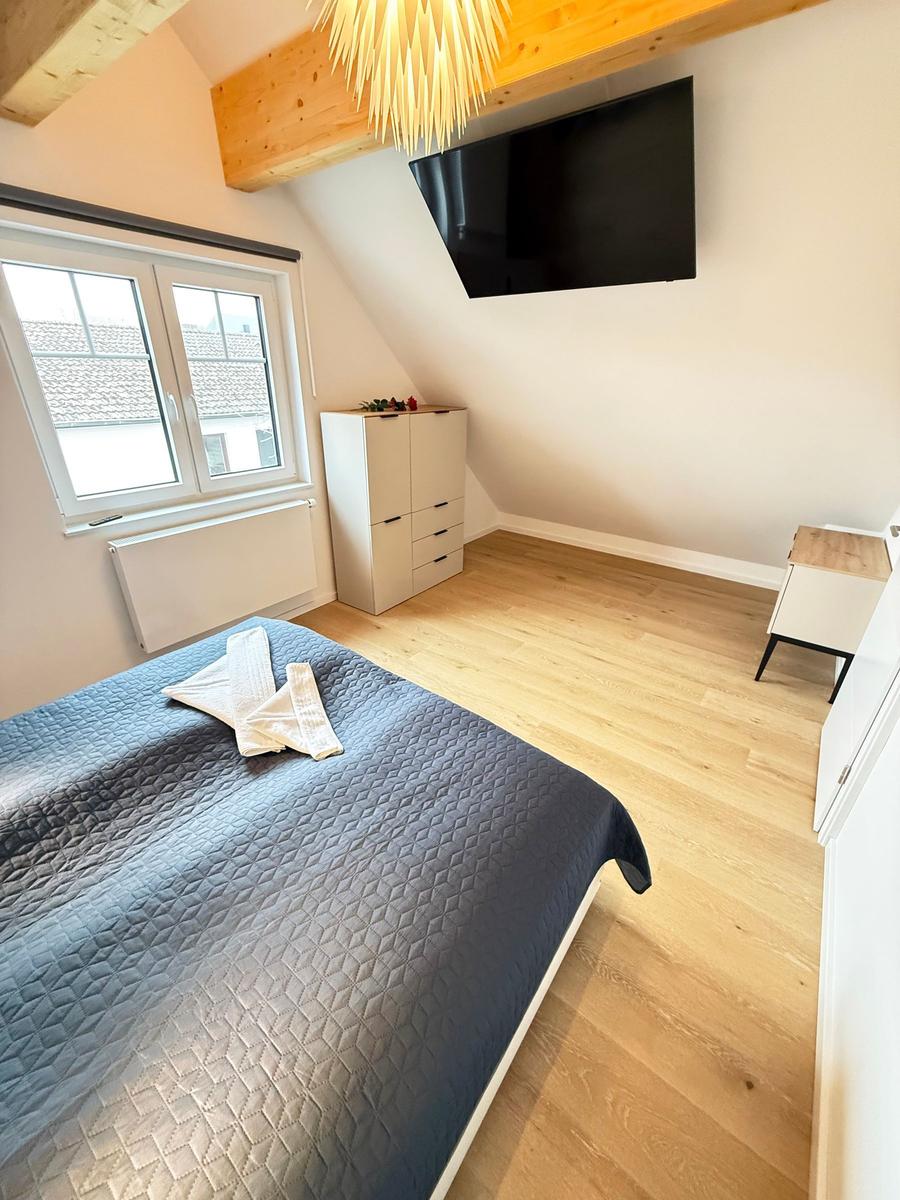 Bedroom with sloped ceiling, bed, wardrobe, and wall-mounted TV.