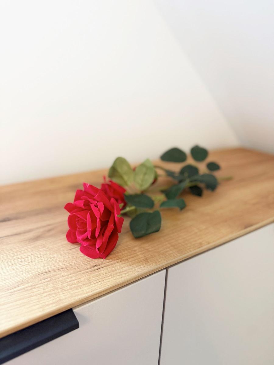 A red rose lies on a wooden surface next to white cabinets.