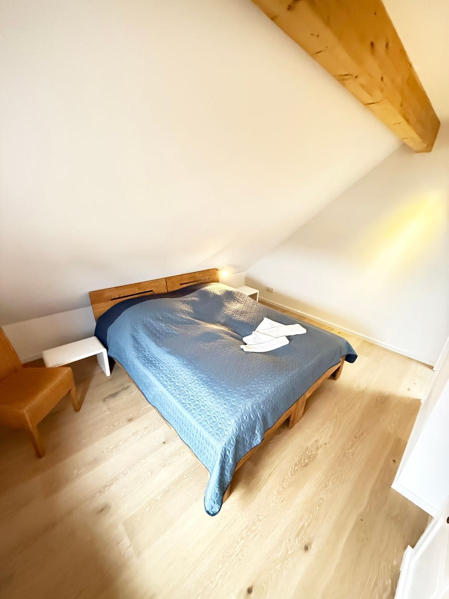 Bedroom with wooden floor, bed, and wooden beam on ceiling.