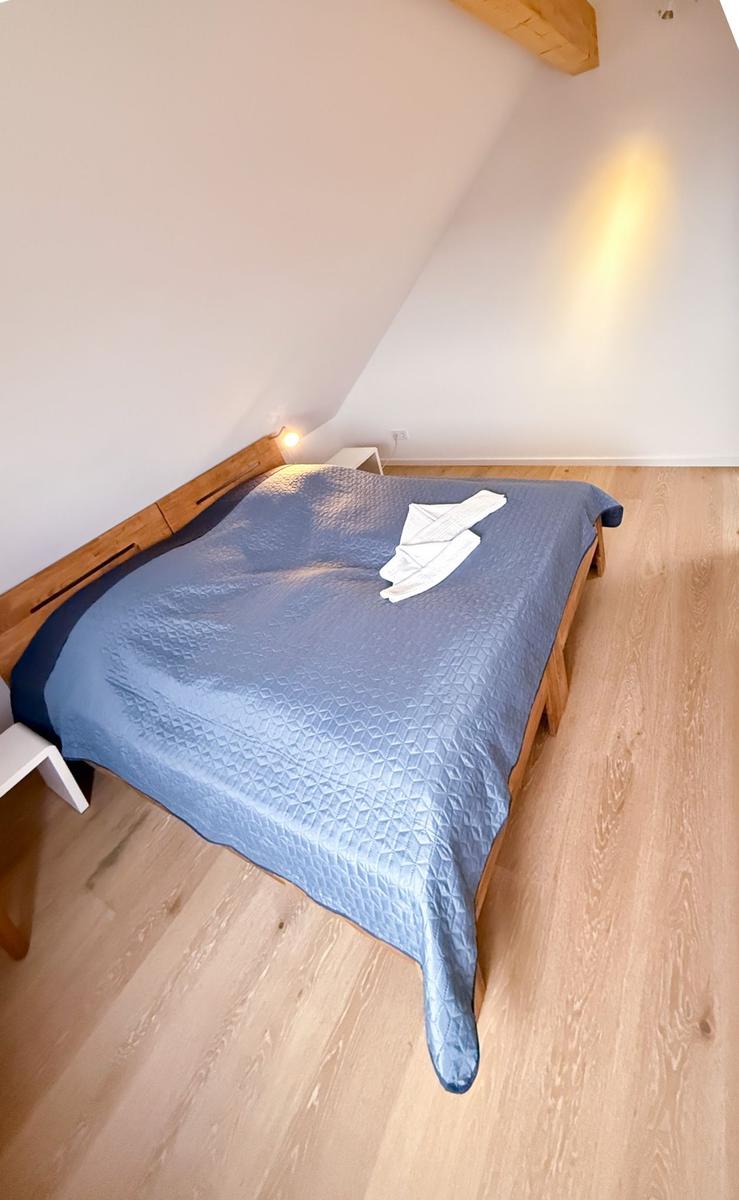Bedroom with wooden floor and sloped ceiling. Bed with blue quilt and white pillows.