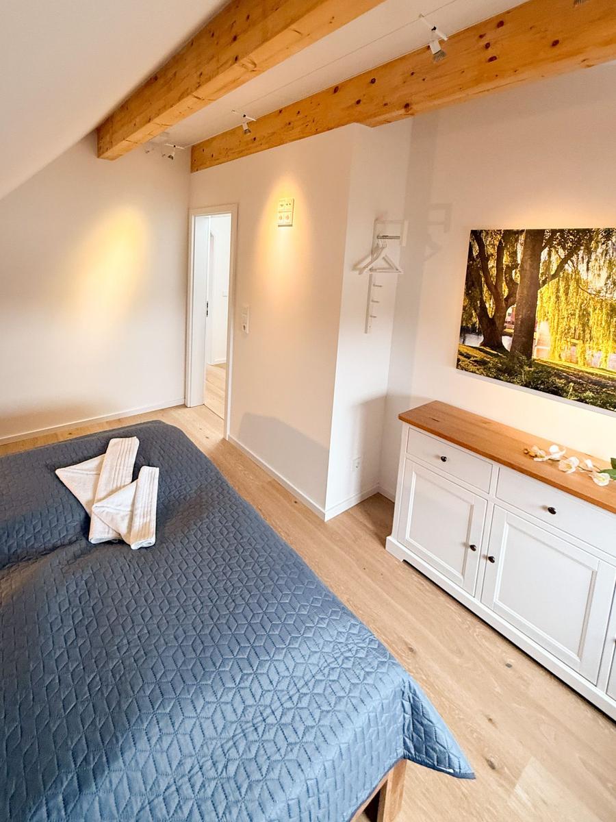 Bedroom with bed, wooden floor, and wall art. Visible ceiling beams and cabinet.
