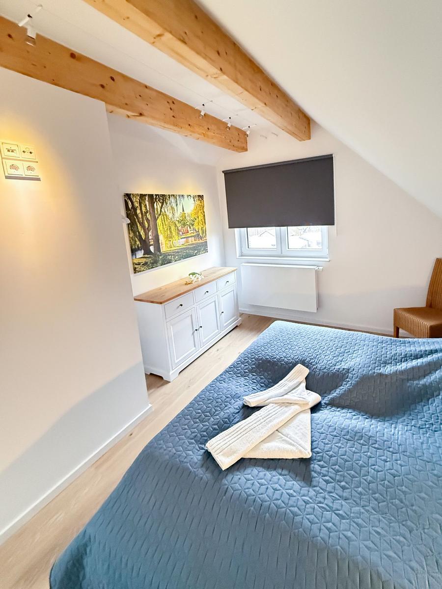 Bedroom with sloped ceiling, wooden beams, bed, and dresser.