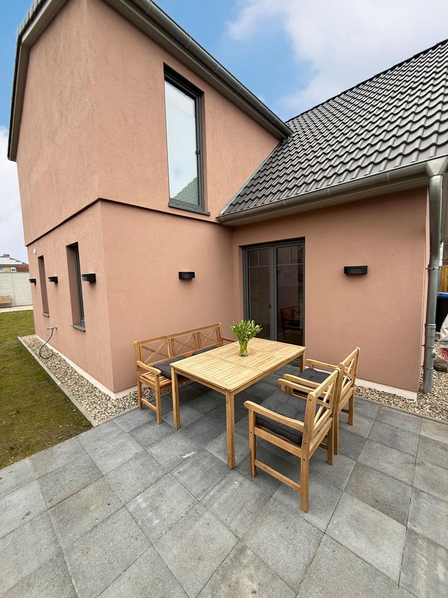 Terrace with wooden table and chairs in front of a house with pink facade.