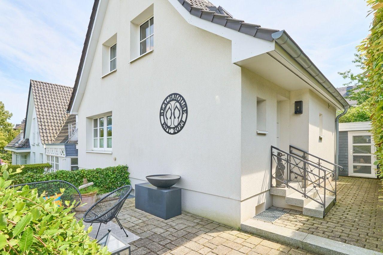 Wohnhaus mit Terrasse, Garten und Eingangstreppe. Außenwand mit Logo.