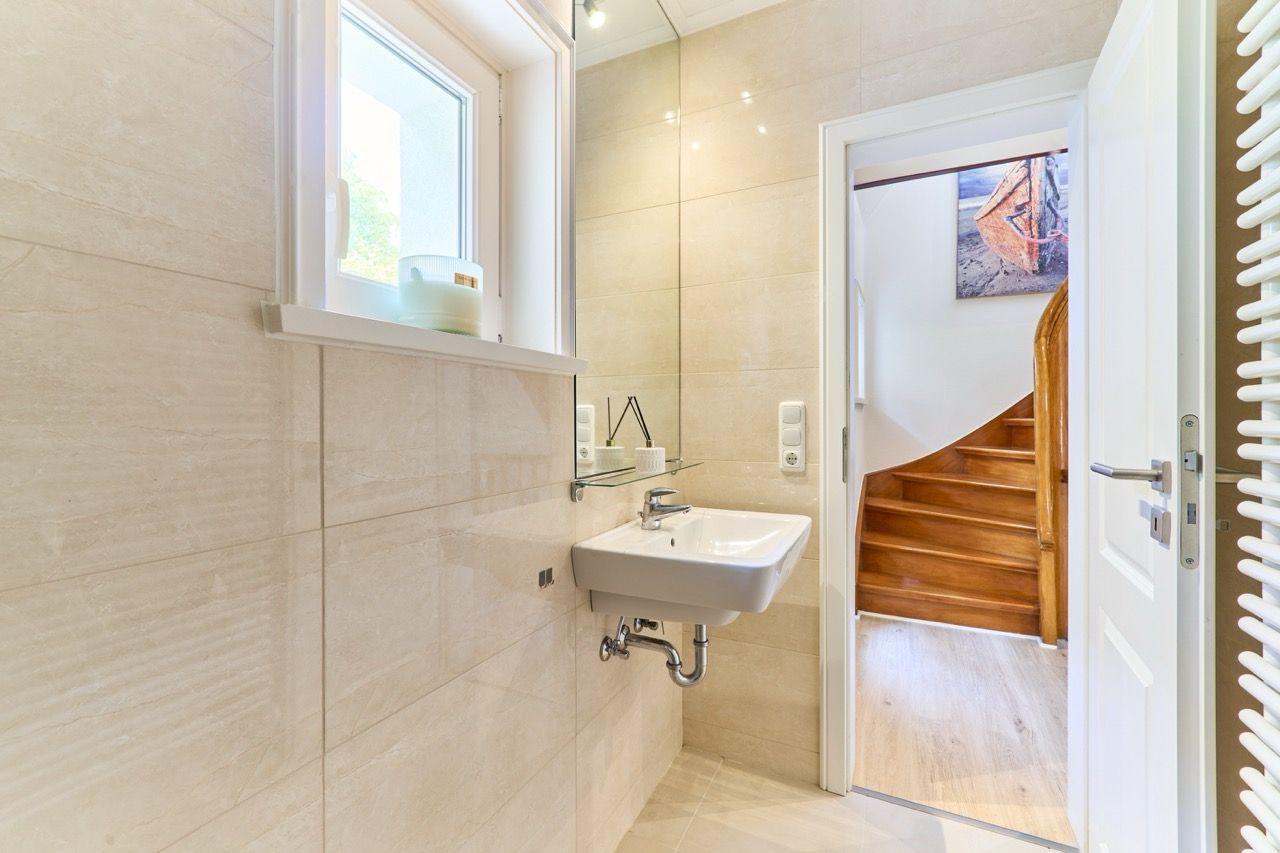 Badezimmer mit Waschbecken, Spiegel und Fenster. Treppe führt in den Flur.
