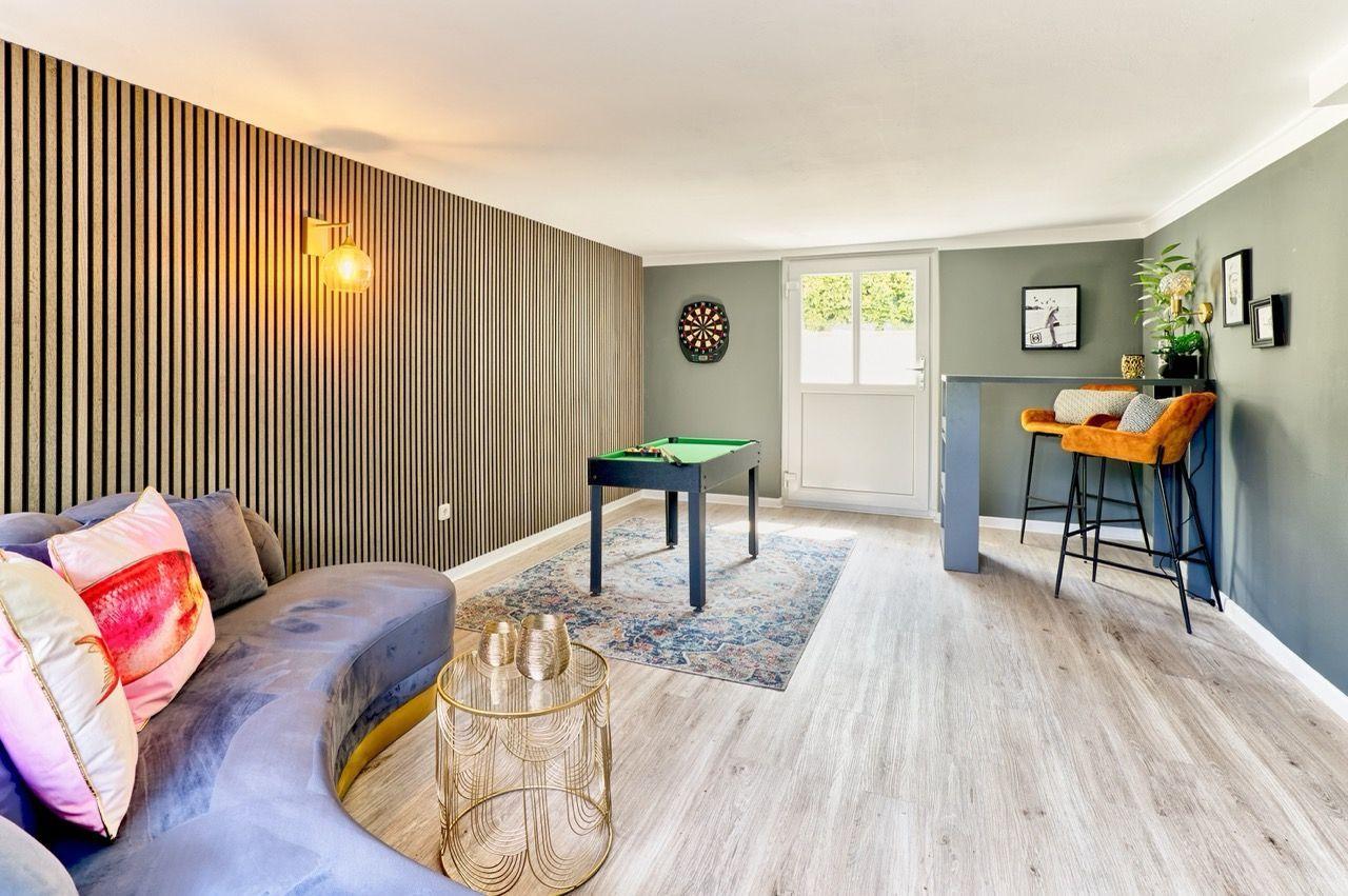 Ein Raum mit Sofa, Billardtisch und Barhockern. Holzwand und Holzboden.