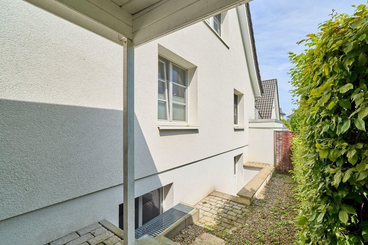 Weiße Fassade mit Fenstern und grüner Hecke im Hintergrund.