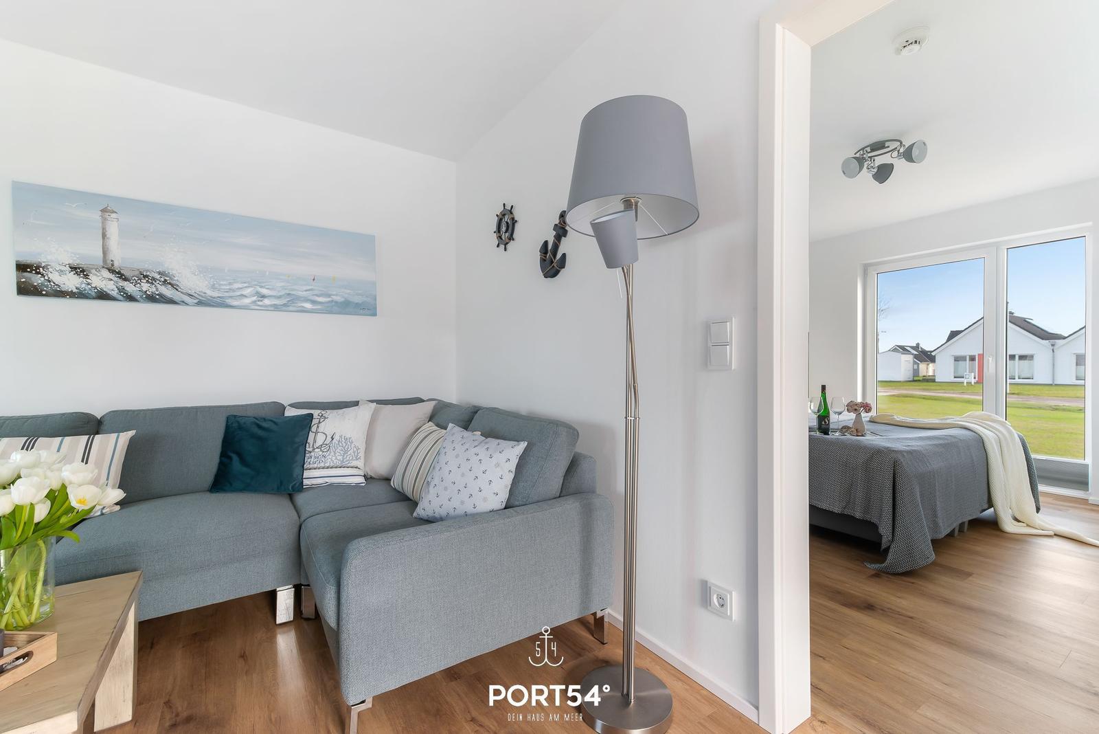 Wohnzimmer mit Sofa und Lampen. Durchgang zur Schlafzimmer mit Bett und Fenster.