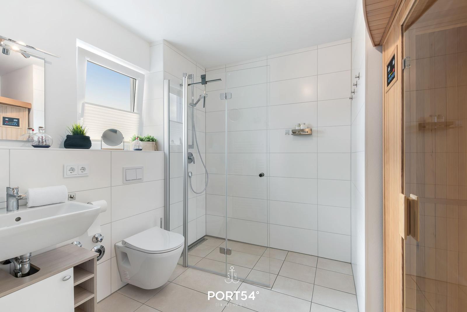 Badezimmer mit Dusche, Waschbecken und Toilette. Sauna im Anschluss.