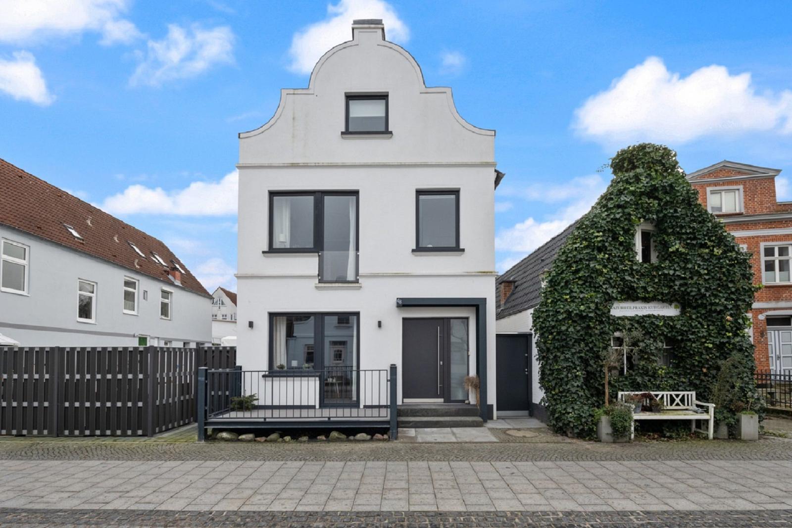 Weißes Haus mit dunklen Fenstern und Eingangstür. Vordere Terrasse und gepflasterter Hof.