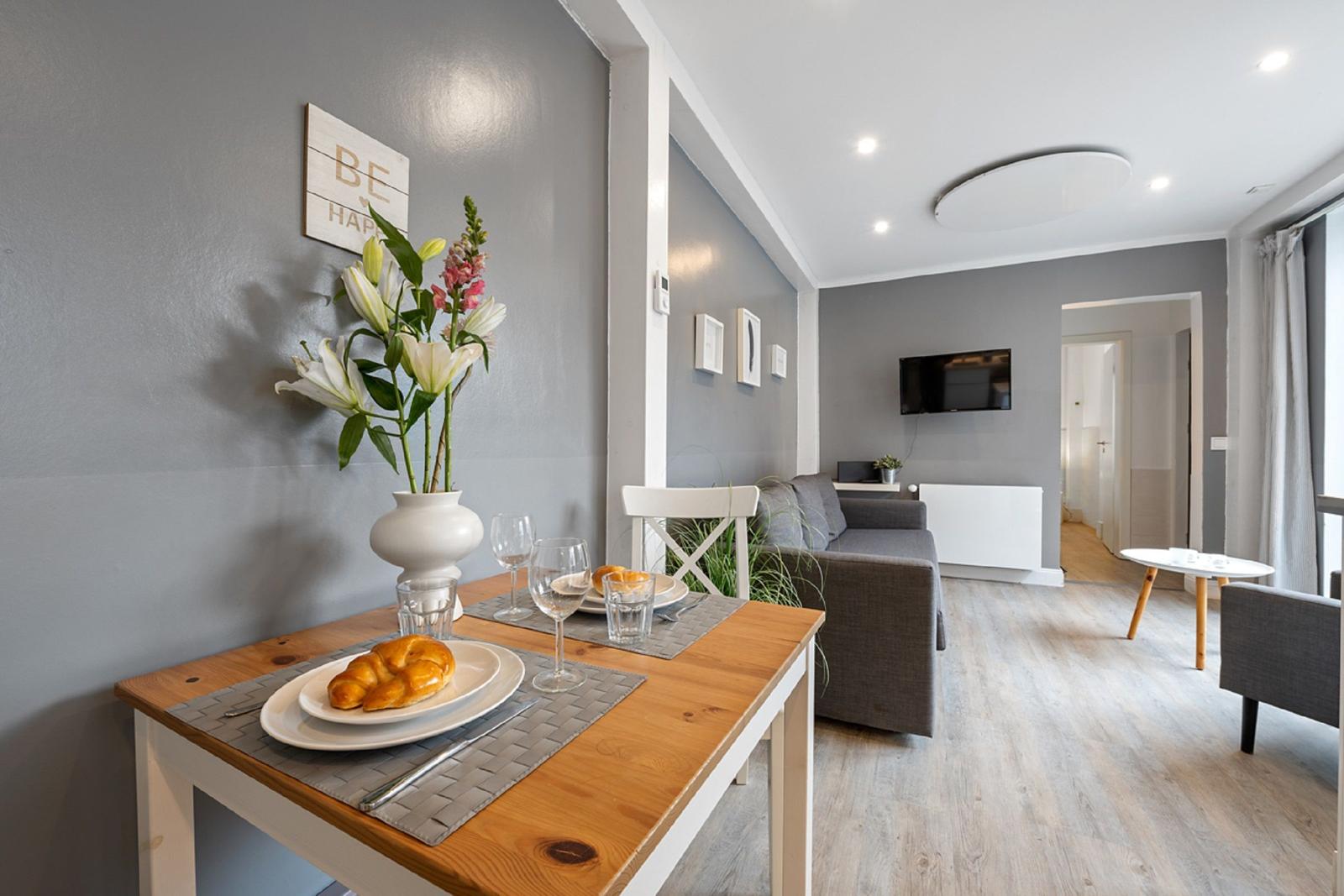 Esszimmer mit Tisch, Stühlen und Blumen. Wohnzimmer mit Sofa und Fernseher.